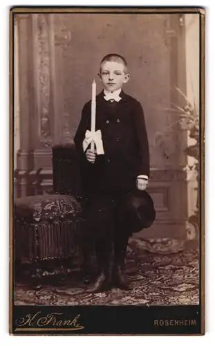 Fotografie K. Frank, Rosenheim, Portrait Knabe im dunklen Anzug mit Hut und Kerze in der Hand
