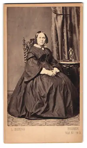 Fotografie L. Herzog, Bremen, Wall 74, Portrait ältere Dame im reifrock Kleid mit Korkenziherlocken, Tischglocke
