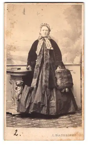 Fotografie L. Bachrich, Wien, Portrait ältere Dame im reifrock Kleid mit Samtmantel und Muff, Habe
