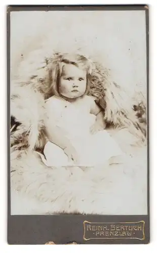 Fotografie Reinh. Bertuch, Prenzlau, Kleinkind mit langen Haaren auf einem Fell