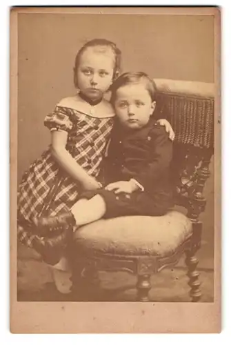 Fotografie Wilh. Dreesen, Flensburg, Norderstrasse 148, Mädchen in kariertem Kleid mit kleinem Bruder auf einem Stuhl