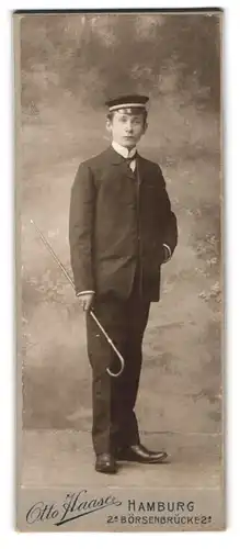 Fotografie Otto Haase, Hamburg, Portrait junger Student im Anzug mit Schirmmütze udn Flanierstock