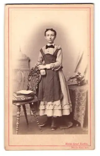 Fotografie Heinr. Graf, Berlin, Friedrich-Str. 165, Portrait junges Mädchen im hellen Kleid mit Schürze und Schleife