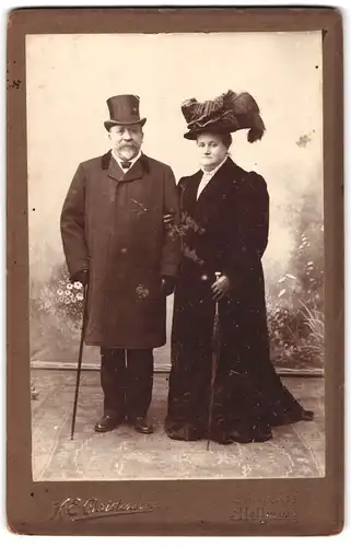 Fotografie H. E. Christensen, Hellerup, Portrait älterer Herr und Dame im Samtmantel mit Federhut und Anzug mit Zylinder
