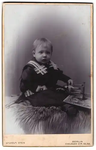 Fotografie Wilhelm Stein, Berlin, Chauseestr. 65-66, Süsses Kleinkind im Kleid mit Spielzeugpferd sitzt auf Fell