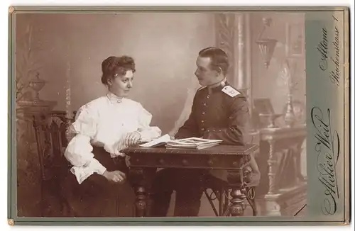Fotografie Atelier Weil, Hamburg-Altona, Reichenstrasse 1, Ufz. des 31. Rgts. in Uniform mit seiner Gattin am Holztisch
