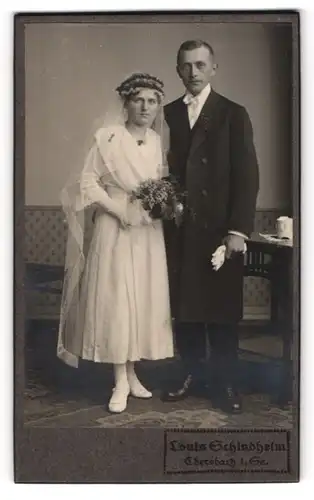 Fotografie Louis Schindhelm, Ebersbach i. Sa., Portrait Eheleute im Hochzeitskleid und Anzug mit Brautstrauss