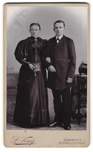 Fotografie L. Kny, Ebersbach i. Sa., Portrait Eheleute zur Hochzeit im schwarzen Kleid und Anzug mit Bibel und Zylinder