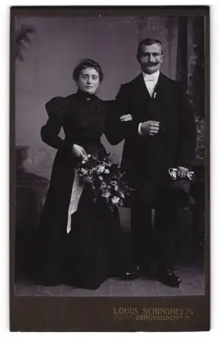 Fotografie Louis Schindhelm, Ebersbach i. Sa., Portrait Brautpaar im schwarzen Hochzeitskleid und Anzug mit Brautstrauss