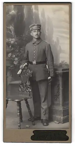 Fotografie August Bies, Hannover, Soldat in Uniform mit Bajonett & Schlagband vor Studiokulisse