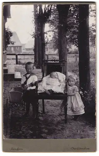 Fotografie Jacobsen, Charlottenburg, Zwei kleine Kinder mit Täufling auf einem Stuhl im Garten