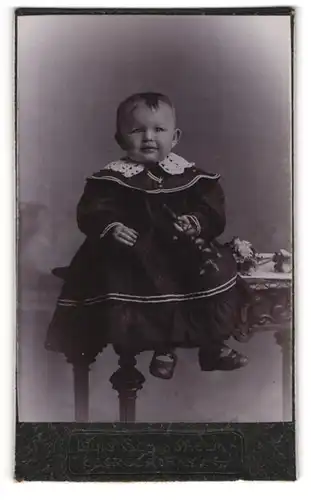 Fotografie Louis Schindhelm, Ebersbach i /S., Kleines Kind im Kleid mit einer Rassel