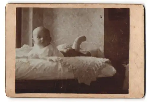 Fotografie unbekannter Fotograf und Ort, Halbnacktes Kleinkind liegt bäuchlings auf einer Decke