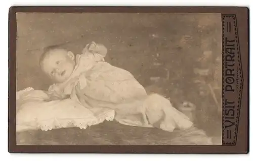 Fotografie unbekannter Fotograf und Ort, Süsses Kleinkind im Kleid liegt auf einem Kissen
