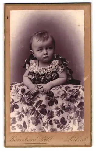 Fotografie Bernhard Prill, Lübeck, Breitestrasse 97, Baby in gerüschtem Kleidchen mit eigensinnigem Blick