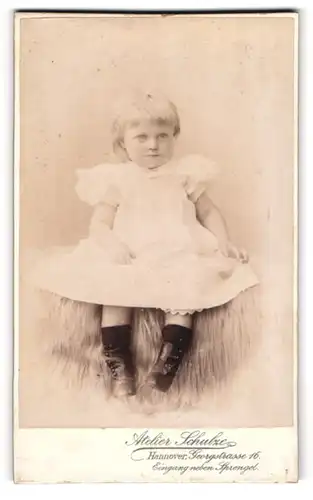 Fotografie Atelier Schulze, Hannover, Georgstrasse 16, Kleines Kind im weissen Kleidchen und Stiefeln auf einem Fell