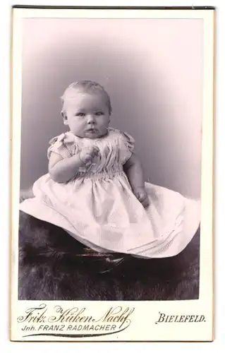 Fotografie Fritz Küken, Bielefeld, Portrait niedliches Baby im hübschen Kleidchen