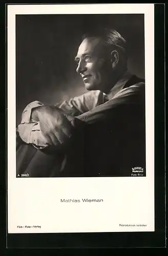 AK Schauspieler Mathias Wiemann mit angezogenen Beinen lächelnd