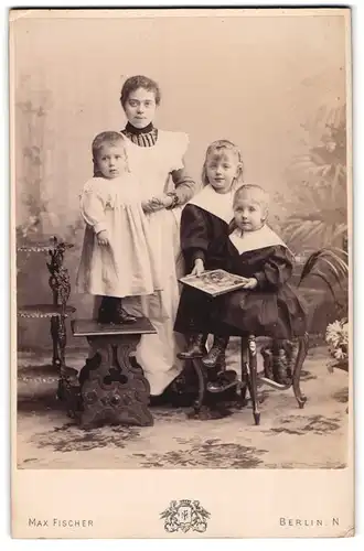 Fotografie Max Fischer, Berlin-N., Invalidenstr. 164, Junge Dame im Kleid und drei Kleine Mädchen mit Bilderbuch