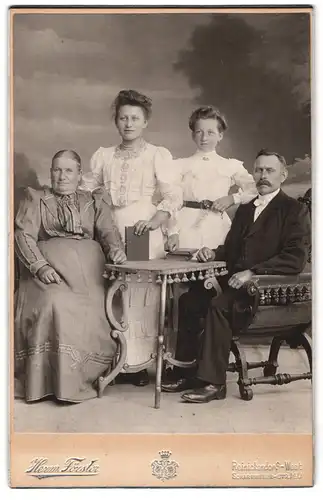 Fotografie Herm. Förster, Reinickendorf-West, Scharnweberstr. 140, Bürgerliches Paar mit zwei älteren Töchtern am Tisch