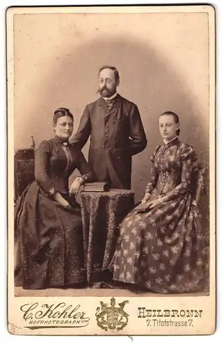 Fotografie C. Kohler, Heilbronn, Titotstr. 7, Bürgerliches Paar und ältere Tochter mit Buch am Tisch