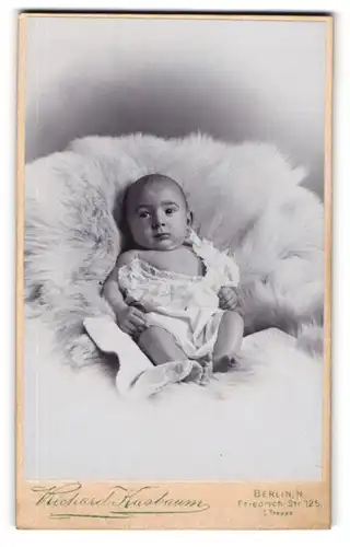Fotografie Richard Kasbaum, Berlin-N., Friedrich-Str. 125, Süsses Kleinkind im Hemd liegt auf Fell