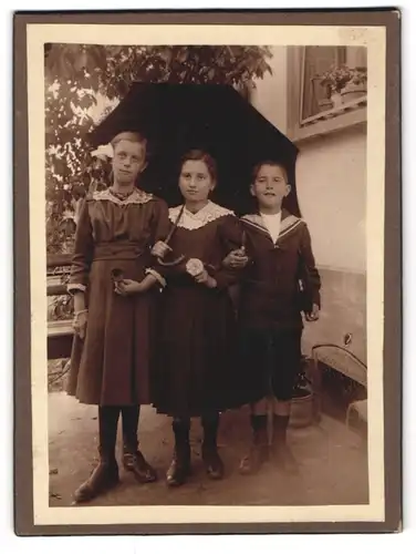 Fotografie unbekannter Fotograf und Ort, Zwei junge Mädchen in Kleidern und Junge unterm Schirm