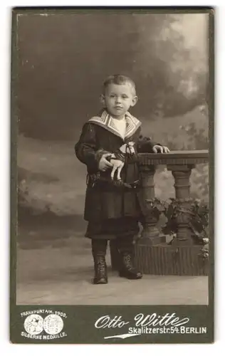 Fotografie Otto Witte, Berlin, Skalitzerstr. 54, Portrait frecher blonder Bube mit Spielzeug in der Hand