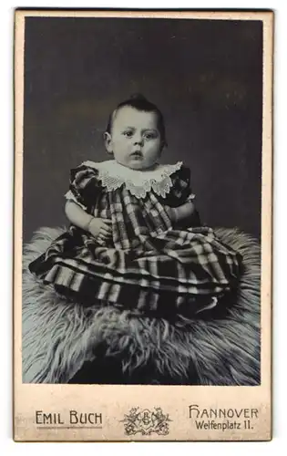 Fotografie Emil Buch, Hannover, Welfenplatz 11, Portrait süsses Baby im karierten Kleidchen auf Fell sitzend