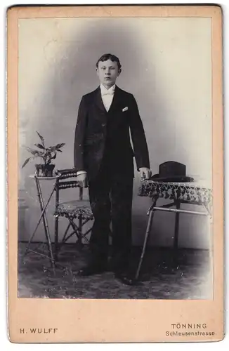 Fotografie H. Wulff, Tönning, Schleusenstr., Junger Mann mit weisser Fliege und Einstecktuch steht neben Tisch