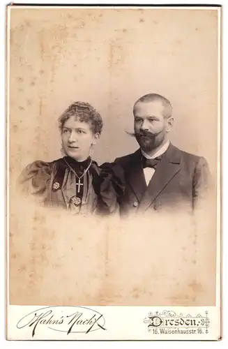 Fotografie Hahns Nachf., Dresden, Waisenhaustr.16, Mann mit aufgestelltem Schnurrbart und Dame mit Kreuzanhänger