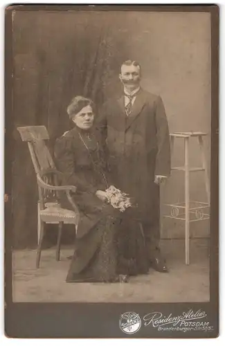 Fotografie REsidenz Atelier, Potsdam, Mann mit dichtem Schnauzbart und sitzende Dame mit Blumenstrauss
