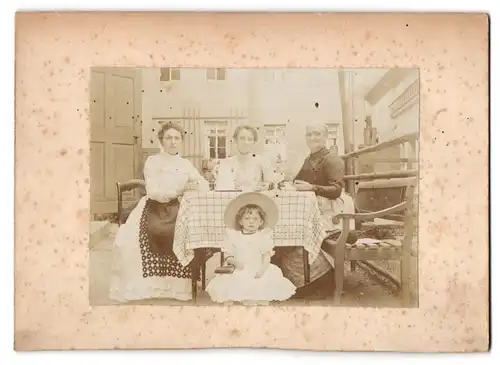 Fotografie Fotograf unbeaknnt, Ort unbekannt, Ältere Dame mit zwei jungen Frauen und Mädchen am Tisch