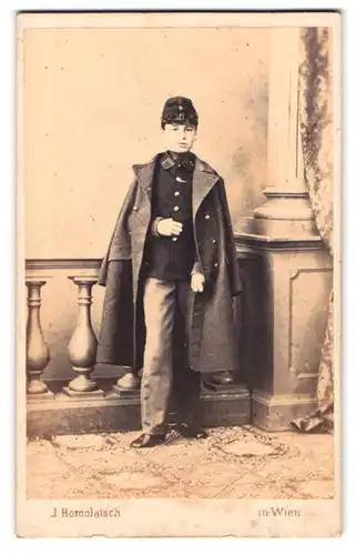Fotografie J. Homolatsch, Wien, Portrait junger Knabe als Kadett in Uniform mit Mantel poisert im Atelier
