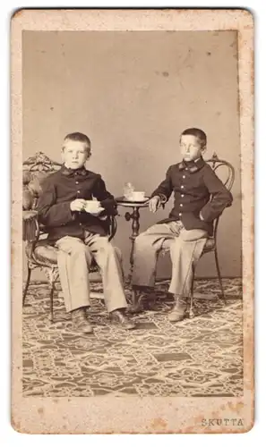 Fotografie Skutta, Wien, Portrait zwei junge Knaben als Kadetten in Uniform beim Kaffeekranz