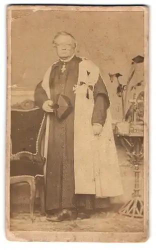 Fotografie unbekannter Fotograf und Ort, älterer Pfarrer im Talar mit Mütze