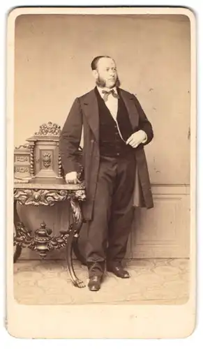 Fotografie G. Ch. Hahn, Dresden, Portrait Herr im dunklen Anzug mit Fliege und Backenbart stehend am Sekretär