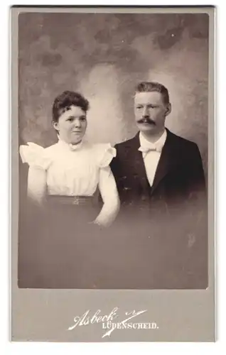 Fotografie August Asbeck, Lüdenscheid, Carlsplatz 11, Lächelnde junge Dame in Rüschenbluse und Herr mit Schnauzer