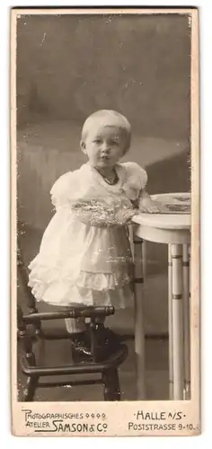 Fotografie Atelier Samson & Co, Halle, Poststrasse 9-10, Kleinkind mit weissem Kleid steht auf Stuhl