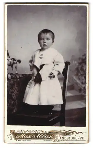 Fotografie Maxbbass, Landstuhl i. Pf., Kind mit kurzen Haaren im Kleidchen auf einem Stuhl