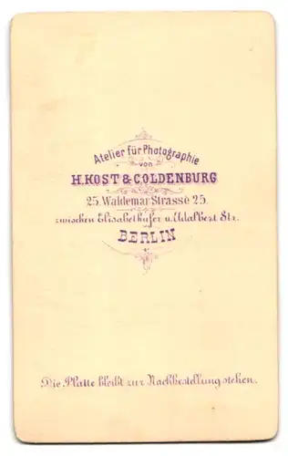Fotografie H. Kost & C. Oldenburg, Berlin, Waldemar Strasse 25, Knirps im edlen Kostüm an einem Tisch ein Buch lesend