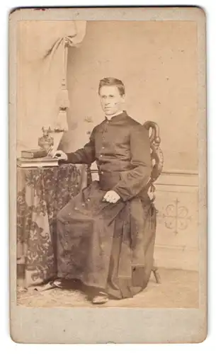 Fotografie Albert Knauf, Eichstaett, Portrait junger Pastor im Talar sitzend im Atelier