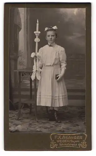 Fotografie F. X. Asanger, Weiden, Bahnhofstr., Mädchen zu ihrer Kommunion mit Kerze im weissen Kleid, Haarschleife