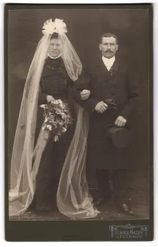 Fotografie Oswald Raspe, Uelzen i. H., Portrait Eheleute im schwarzen Hochzeitskleid mit Schleier und Anzug, Zylinder