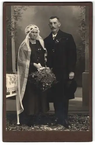 Fotografie unbekannter Fotograf und Ort, Portrait Ehepaar im schwarzen Hochzeitskleid und Anzug mit Brautstrauss