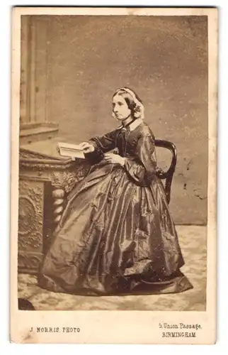 Fotografie J. Norris, Birmingham, 5. Union Passage, Gestandene Dame im seidigen Kleid am Sekretär ein Buch lesend