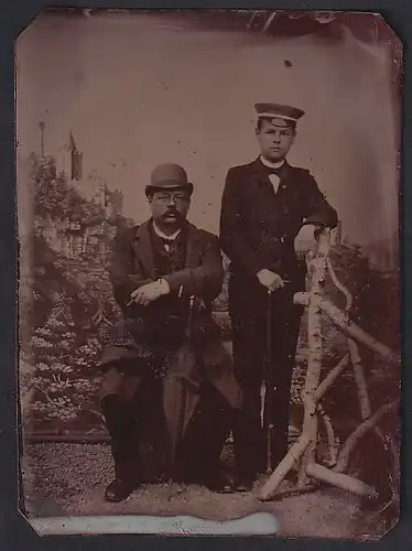 Fotografie Ferrotypie Vater und Sohn in Anzügen posieren vor einer Studiokulisse