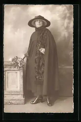 AK Frau im schwarzen Mantel mit einem Hut an einer Säule
