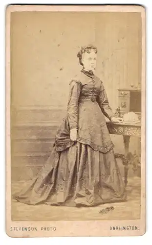 Fotografie Stevenson, Darlington, Junge Frau mit Stirnlocken in tailliertem Rüschenkleid