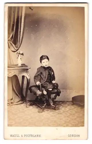 Fotografie Maull & Polyblank, London, 55. Gracechurch Street, Junger Bube im eleganten Kostüm auf einem Hocker sitzend
